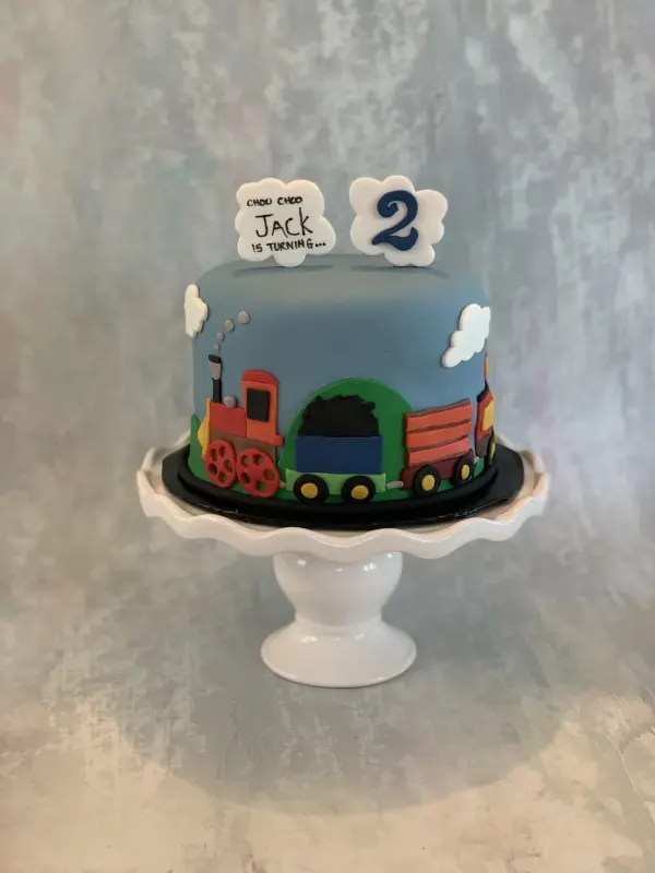 Train birthday cake with cloud plaques reading Choo Choo Jack is turning 2 and a fondant steam engine