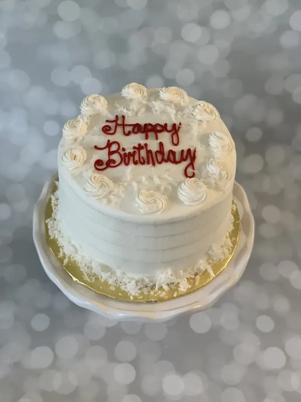 Round white cake with buttercream rosettes, coconut flakes and Happy Birthday piped in red