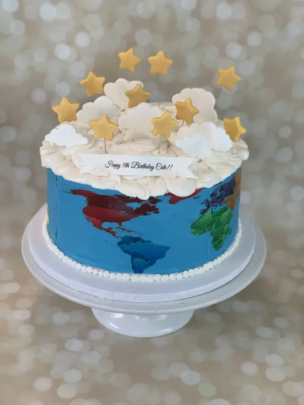 World map birthday cake with buttercream clouds, gold stars and a Happy 5th Birthday Cate banner