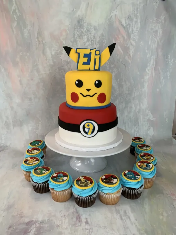 Two-tier Pokemon cake with a Pikachu face tier, Eli topper, number 9 Poke Ball and character cupcakes