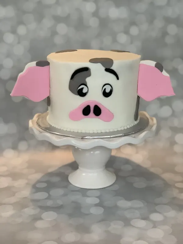 Farm animal face cake with pink fondant ears, a pink snout and grey fondant spots