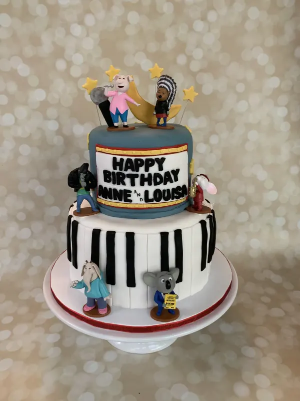 Two-tier Sing movie cake with a piano-key tier, animal singer figures and Happy Birthday Anne and Louisa