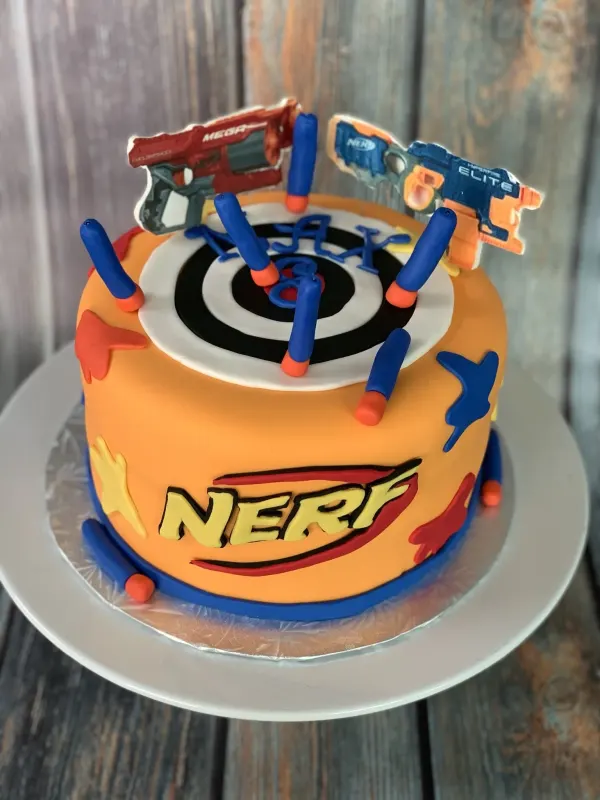 Nerf birthday cake in orange fondant with a bullseye target, foam darts and blaster toppers