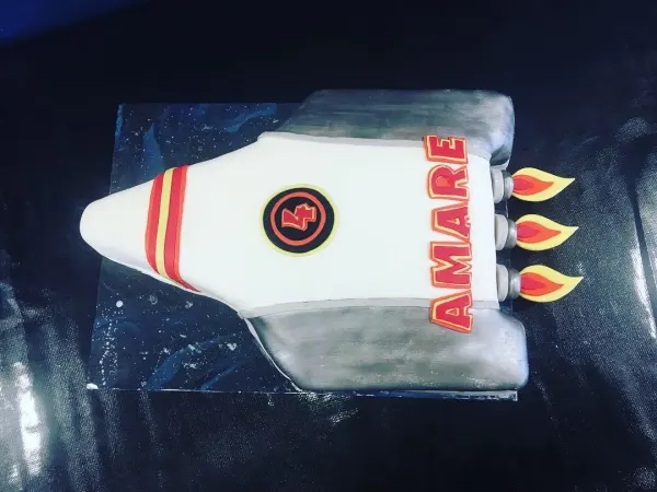 Rocket ship shaped cake in white and silver fondant with AMARE down the side and fondant flames