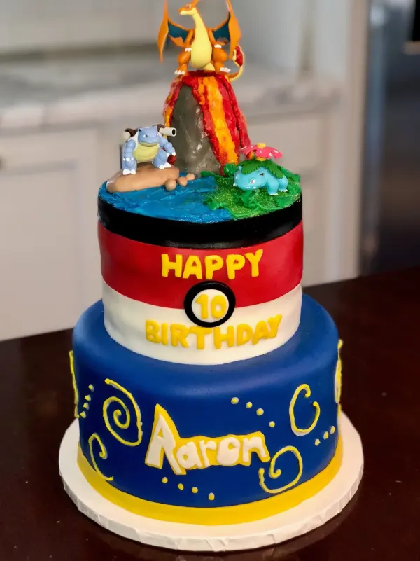 Two-tier Pokemon cake with a Pokeball tier, volcano top and Charizard, reading Happy 10 Birthday Aaron