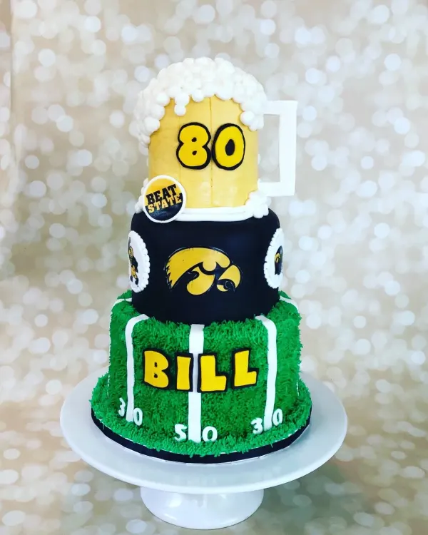 Three-tier Iowa Hawkeyes cake with a beer mug 80 topper and BILL on a piped football field tier