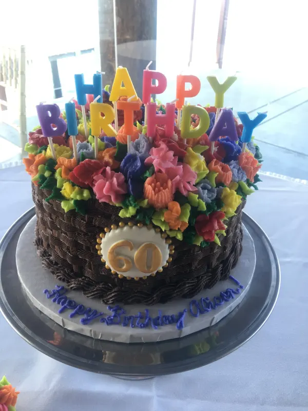 Chocolate basketweave cake topped with piped buttercream flowers, a gold 60 plaque and Happy Birthday Alison