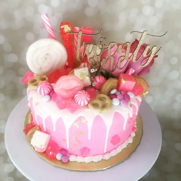 Pink drip cake piled with candy, cookies and gold leaf under a gold twenty one script topper