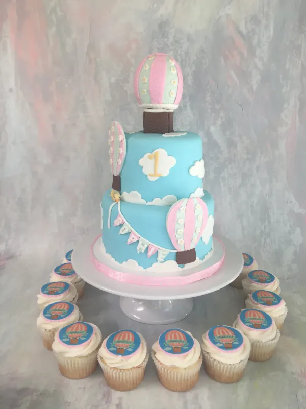 Two-tier hot air balloon first birthday cake in pale blue with a Sophie bunting and matching cupcakes