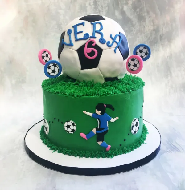 Soccer birthday cake with a fondant soccer ball topper and a girl player on a grass-textured tier