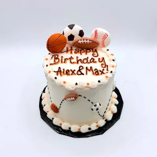 White cake topped with fondant basketball, soccer, football and baseball, lettered Alex and Max
