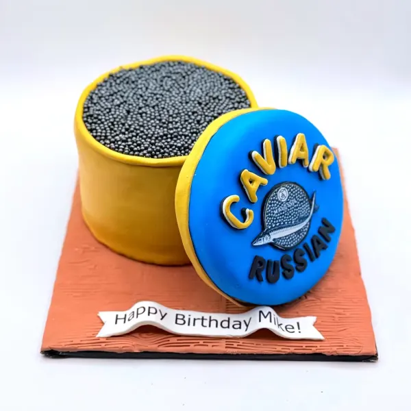 Sculpted caviar tin cake with a blue lid and black sprinkle caviar, on an orange board