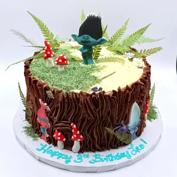 Tree stump cake with piped bark, a mossy top, mushrooms, ferns and troll figures