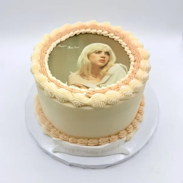 Cream cake with piped shell borders and a round edible print of a singer
