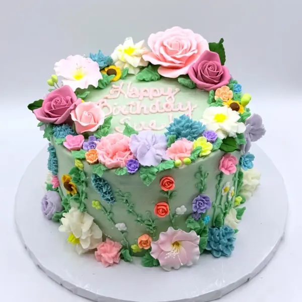 Sage green cake covered in piped buttercream flowers in pink, purple, yellow and blue