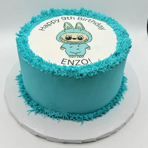 Turquoise cake with piped textured borders and a round edible print of a toothy character