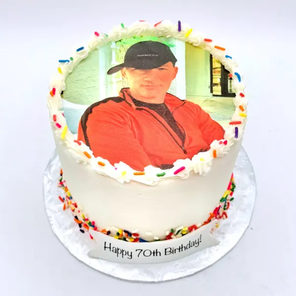 White cake with an edible photo print of a man in a cap, a piped border and rainbow sprinkles