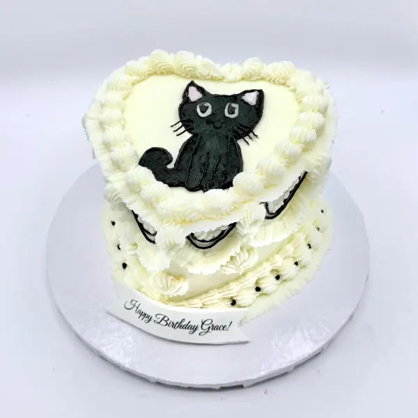 Cream heart shaped cake with a piped black cat and Lambeth borders, lettered Happy Birthday Grace