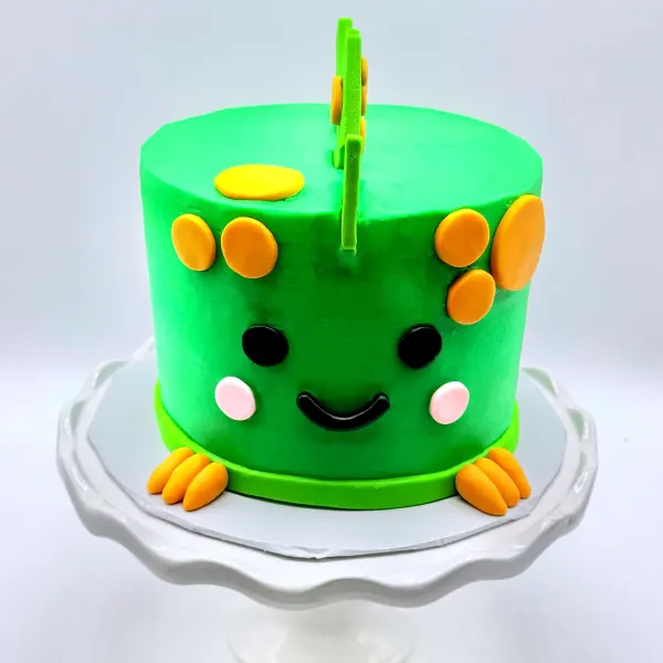 Bright green dinosaur cake with a smiling face, orange fondant feet and a green sprout topper