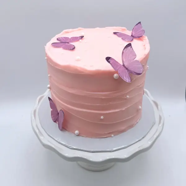 Pink textured buttercream cake with purple fondant butterflies and small pearls