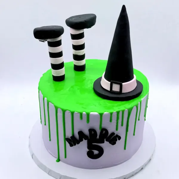 Green and lavender drip cake with a black witch hat and striped witch legs, lettered Margo 5