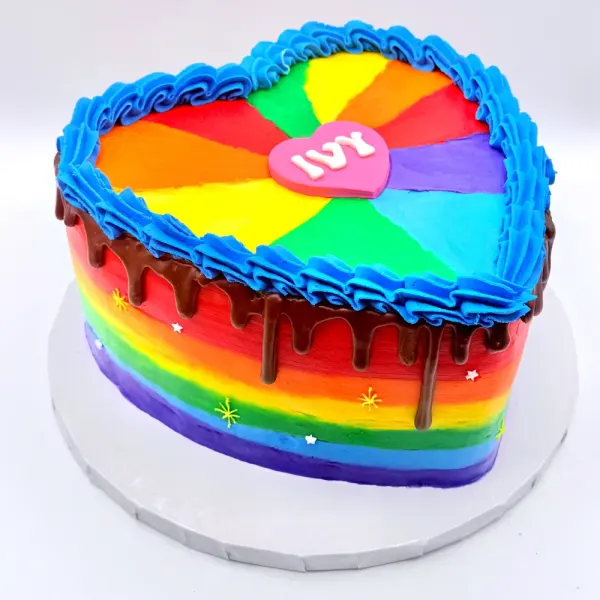 Rainbow striped heart shaped cake with a chocolate drip, a pinwheel top and an Ivy heart plaque