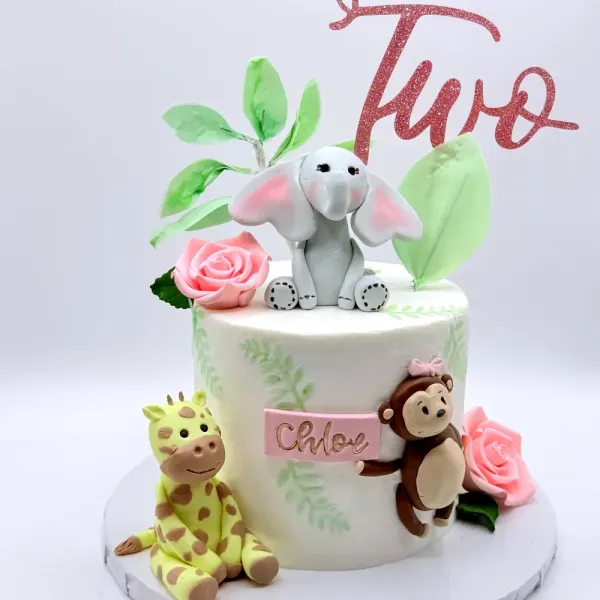 White cake with elephant, giraffe and monkey figures, green leaves, sugar roses and a Chloe plaque