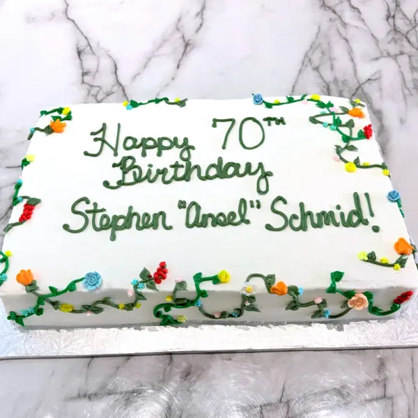 White sheet cake with green vines, small colorful flowers and 70th birthday lettering in green