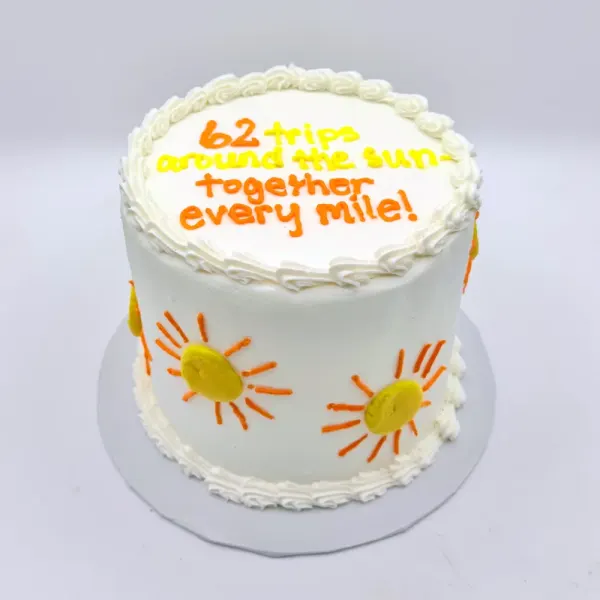 White cake with piped suns around the sides and 62 trips around the sun lettered on top