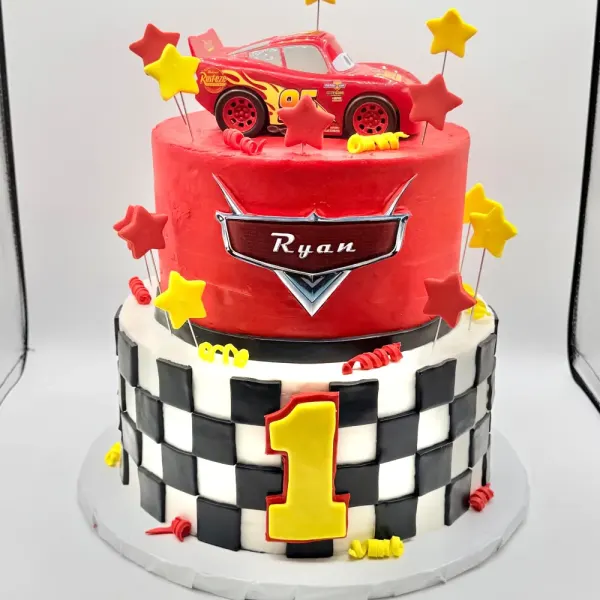 Two tier cake with a race car figure, a Ryan plaque, fondant stars and a checkered flag tier
