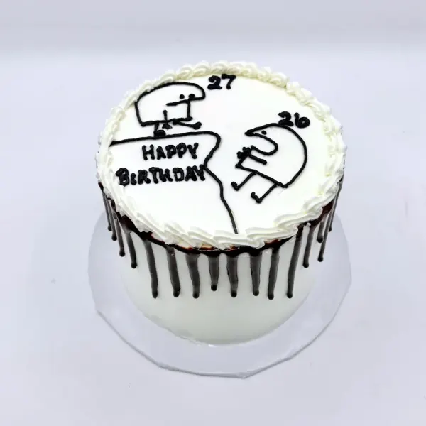 White cake with a chocolate drip and a piped line drawing of two figures with 27 and 26