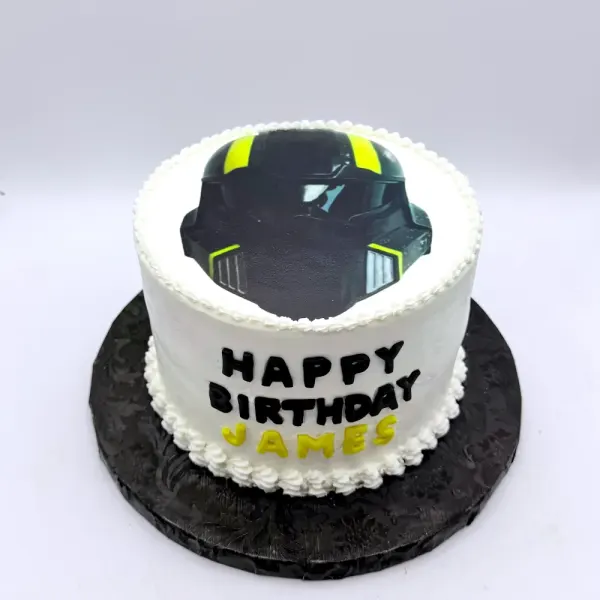 White cake with a black motorcycle helmet on top and Happy Birthday James in black and yellow