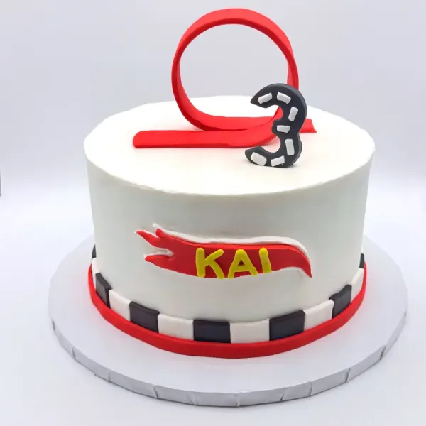 White cake with a red racetrack loop topper, a checkered band and Kai lettered in a red banner