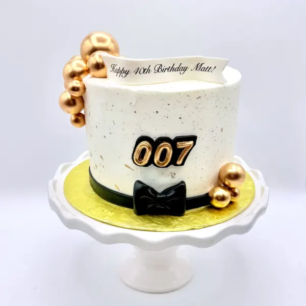 Speckled white cake with gold spheres, a black bow tie and 007 in gold and black