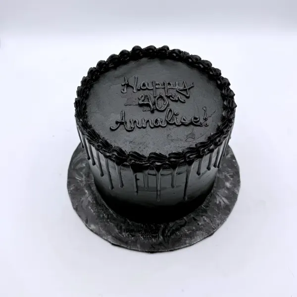 All black cake with a piped shell border and Happy 40th Annalise lettered in black