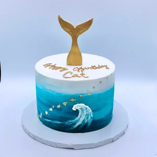 Ocean cake with a gold mermaid tail topper, a hand painted wave and gold flecks