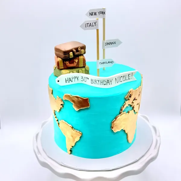 Turquoise cake with gold map continents, stacked fondant suitcases and a signpost of destinations
