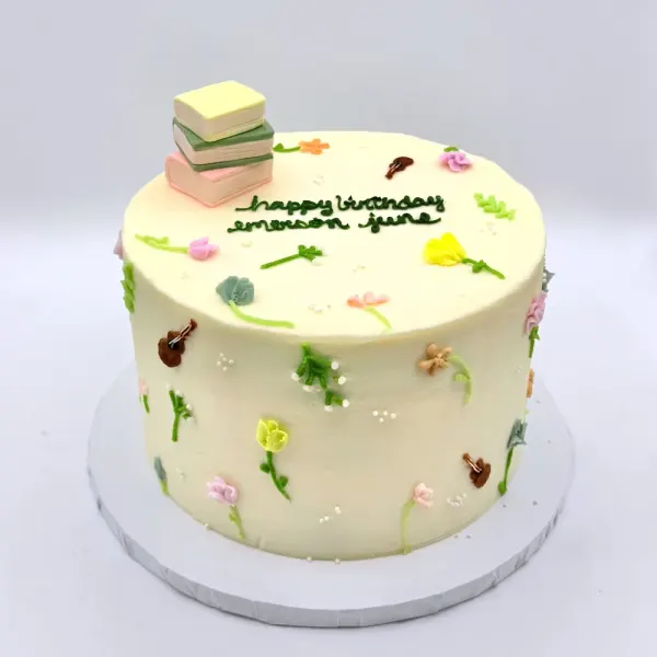 Cream cake with small pressed flowers and violins scattered over it and stacked books on top