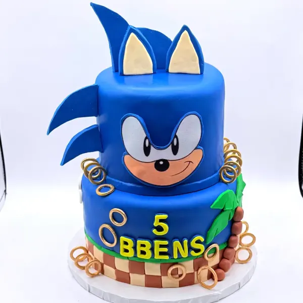Two tier blue cake with a Sonic face and quills, gold rings and a checkered band