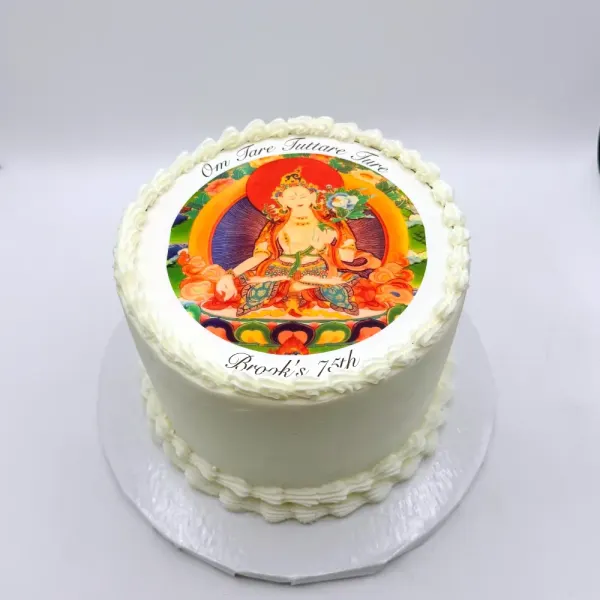 White cake with piped shell borders and a round edible print of a seated deity, lettered Brooks 74th