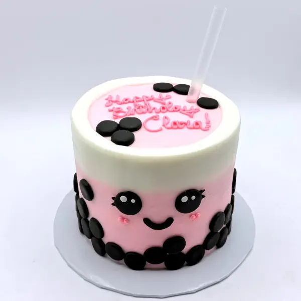 Boba tea cake in pink and cream with black fondant pearls, a smiling face and a straw on top