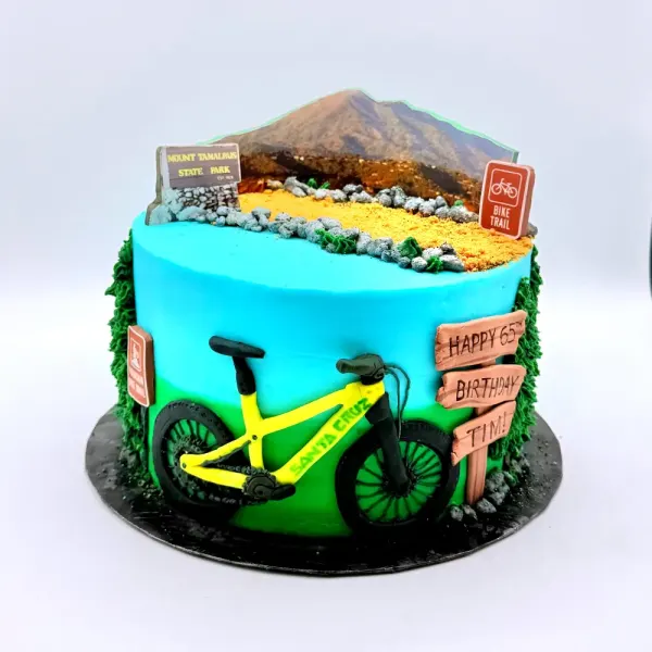 Cake with a mountain landscape top, a yellow mountain bike and wooden trail signs on turquoise