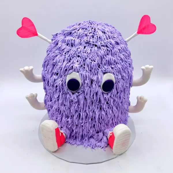Purple monster cake piped to look furry, with googly eyes, heart antennae and fondant shoes