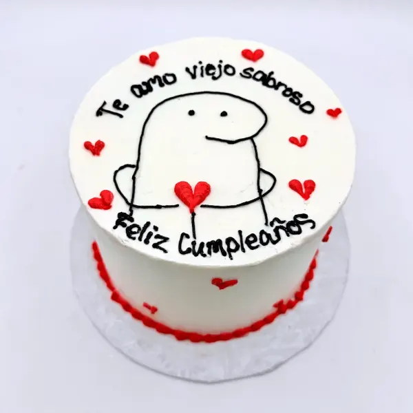 White cake with a hand drawn cartoon figure, red hearts and Feliz Cumpleaños lettered on top