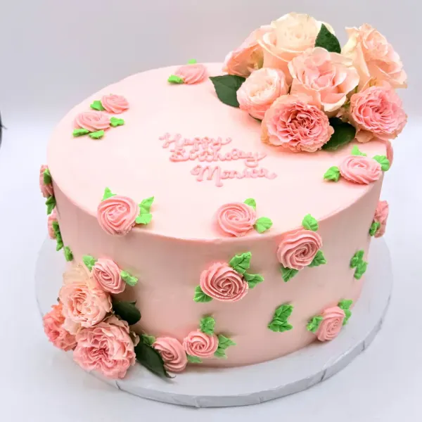 Pink cake with piped roses over the sides and a cluster of peach roses on top