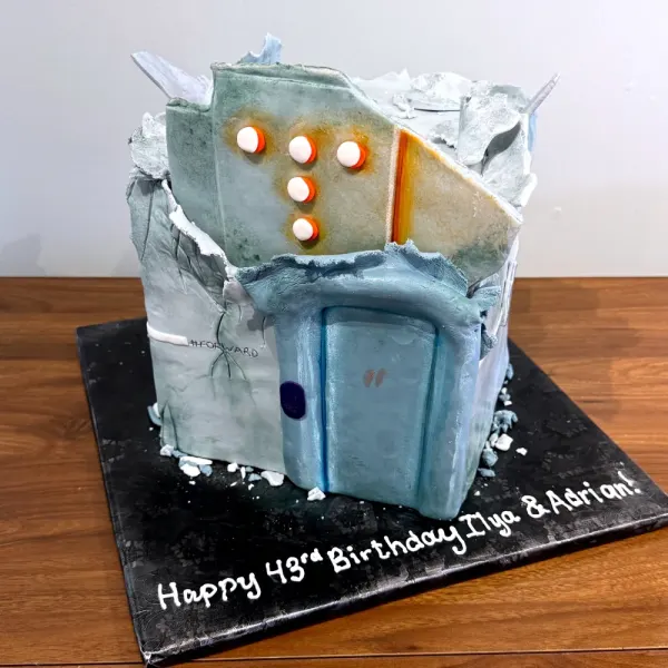 Sculpted cake of a weathered concrete building with a blue door and lit windows, on a black board