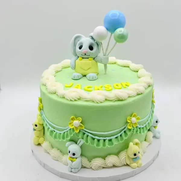 Green cake with a bunny figure holding balloons, small bunnies and flowers, lettered Jackson