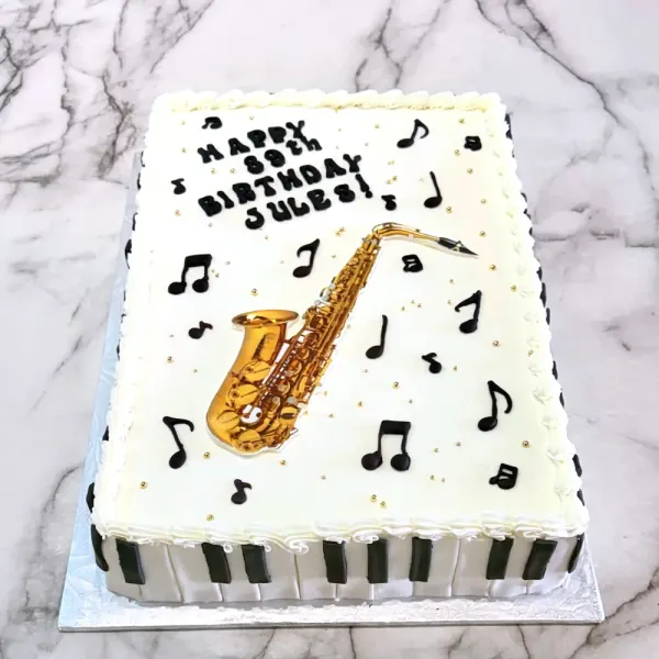 White sheet cake with a gold saxophone, black music notes and a piano key border