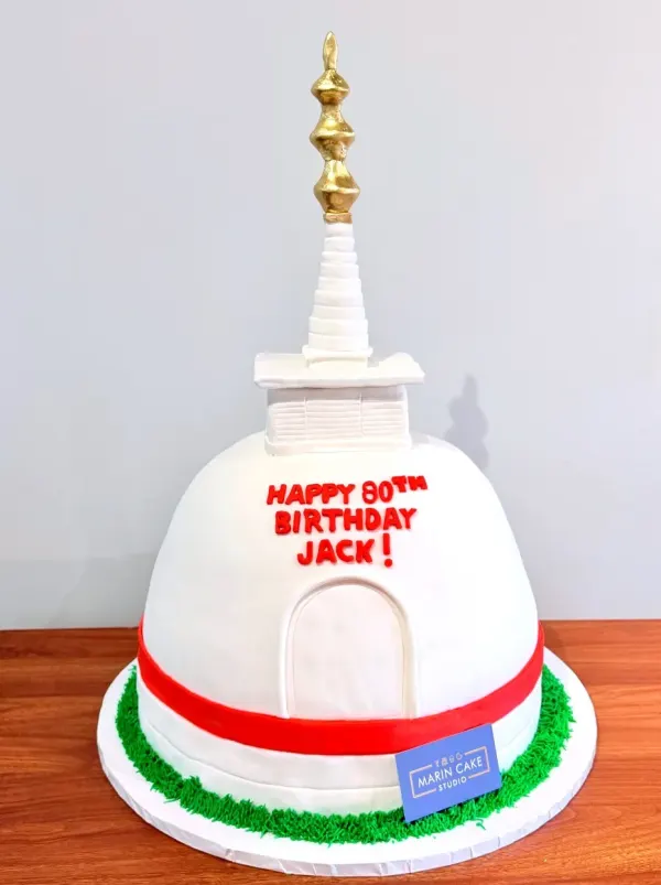 White stupa shaped cake with a gold spire, a red band and 80th birthday lettering in red