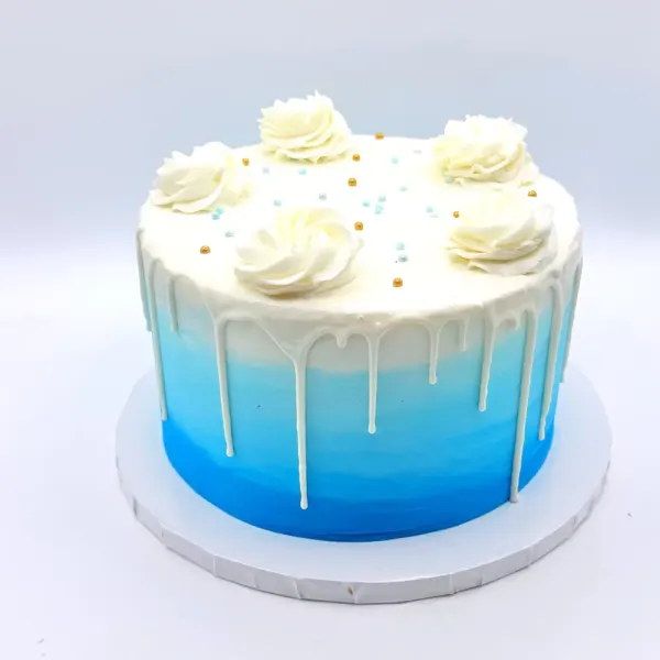 Blue ombré cake with a white drip, piped rosettes and small blue and gold sprinkles